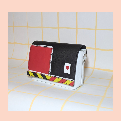 Godot-San maroquinerie rabat "reine de cœur" couleurs principales utilisées : noir, rouge, puis une bande à chevrons jaune, noir et rouge. liseré de dentelle et marqueterie carte blanche avec cœur rouge (comme une carte à jouer) monté sur une poche blanche.